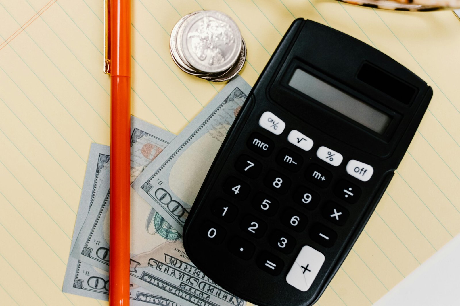 Close-up image of a calculator, pen, and currency on a yellow notepad, symbolizing finance.